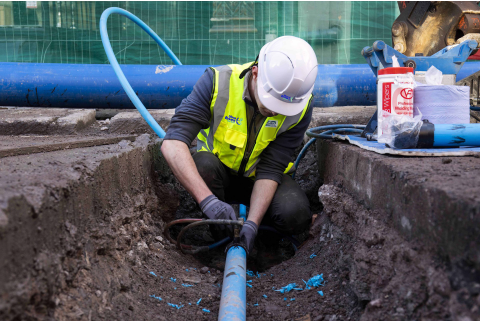 An Uisce Éireann worker fixing a blue pipe in the ground