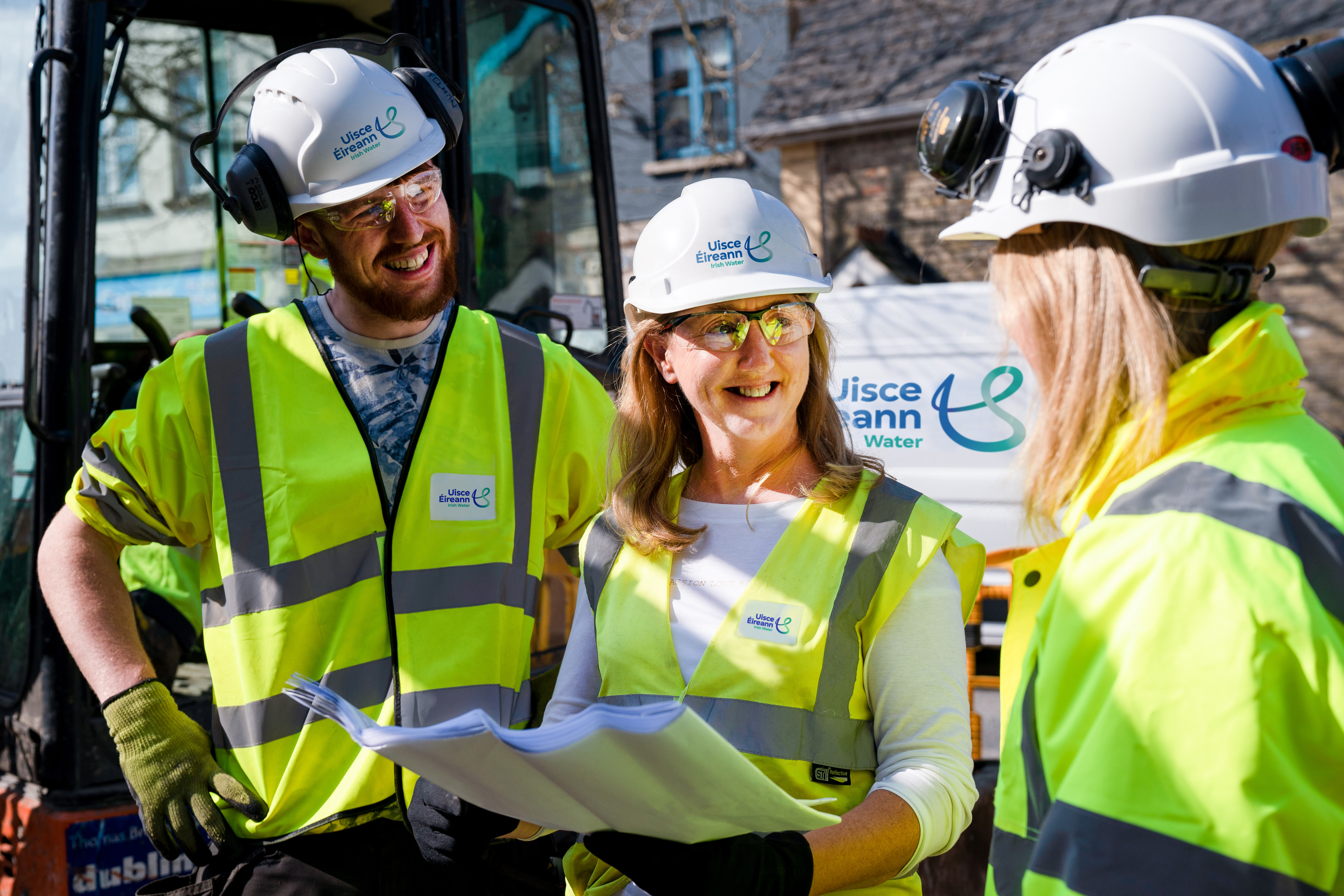 3 Uisce Éireann engineers holding site plans while smiling at eachother