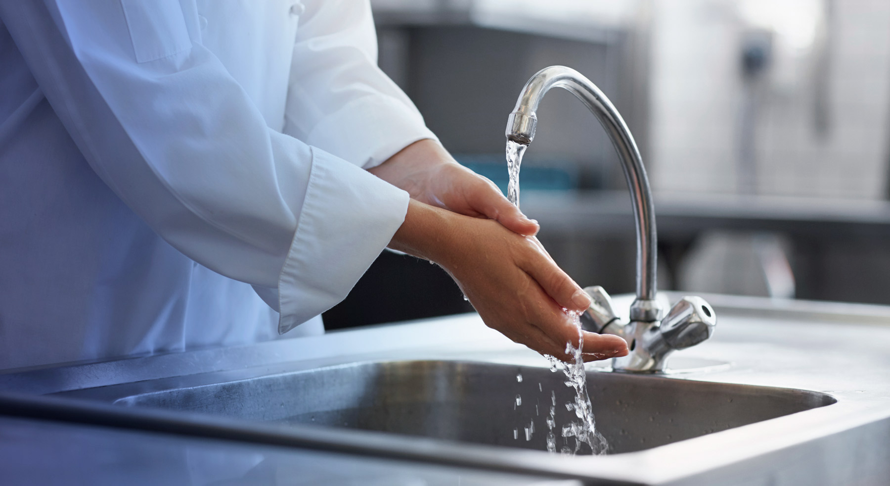 A person washing their hands in a kitchen sink