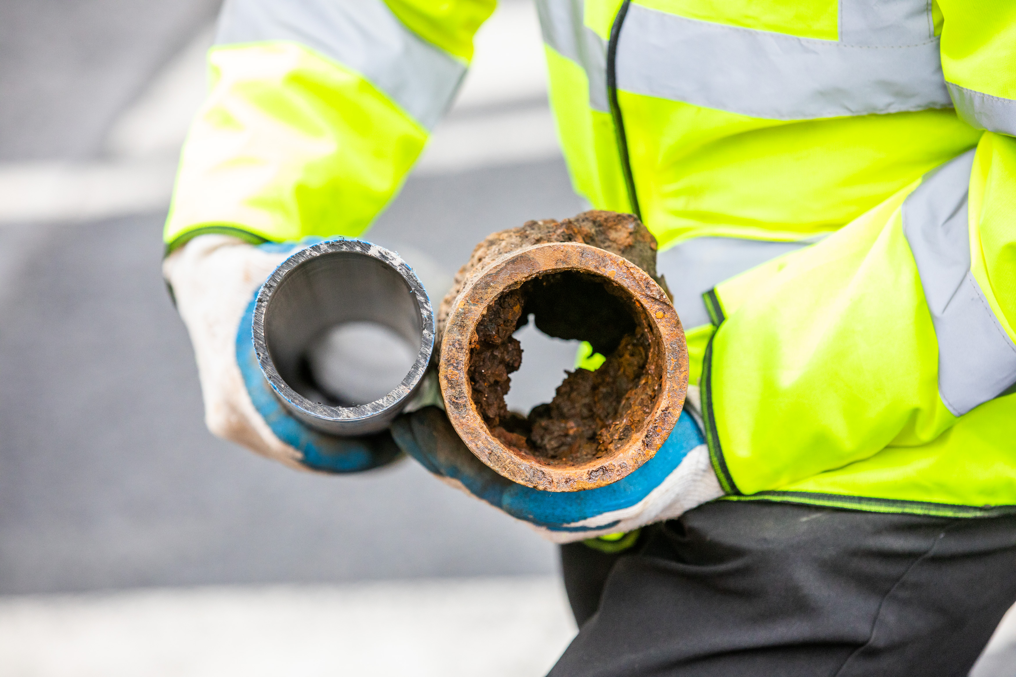 A worker holding a new pipe next to an old and rusty pipe