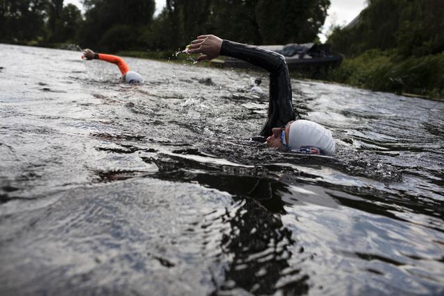 Two swimmers in wetsuits swimming in a river