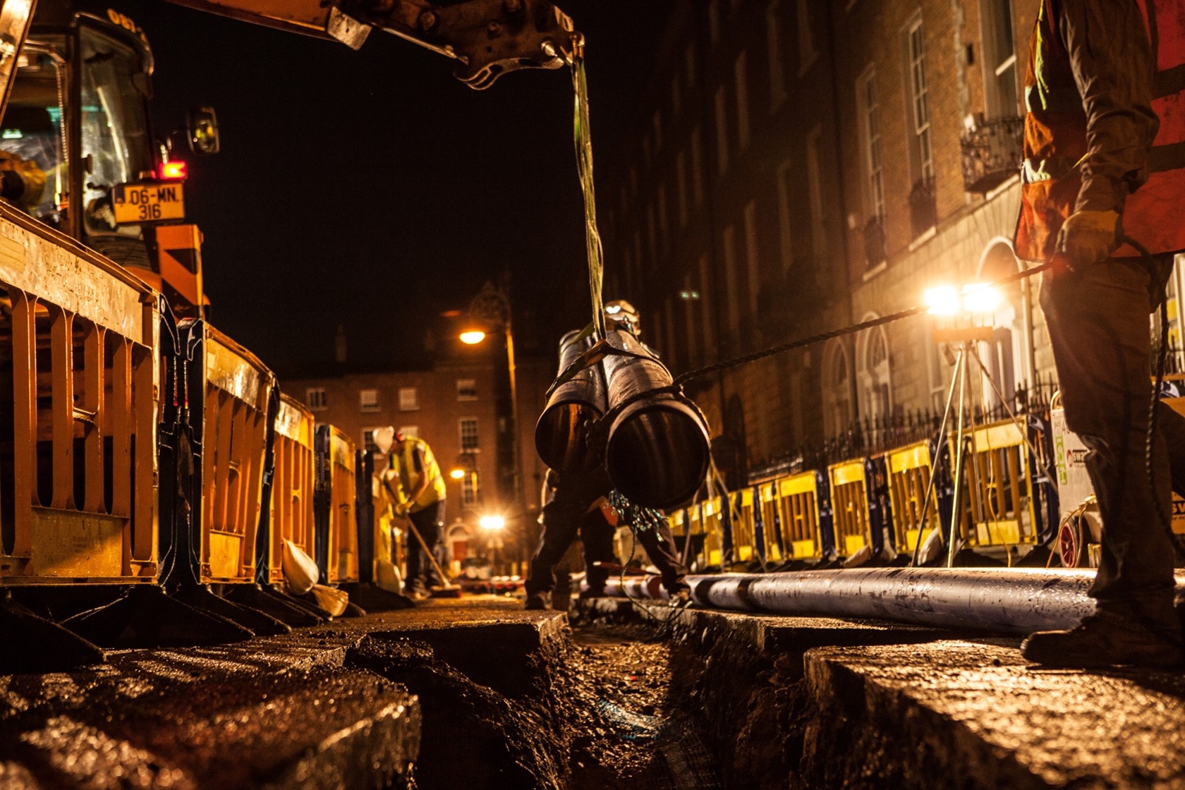 Uisce Éireann workers lowering pipes into the ground on a street at night