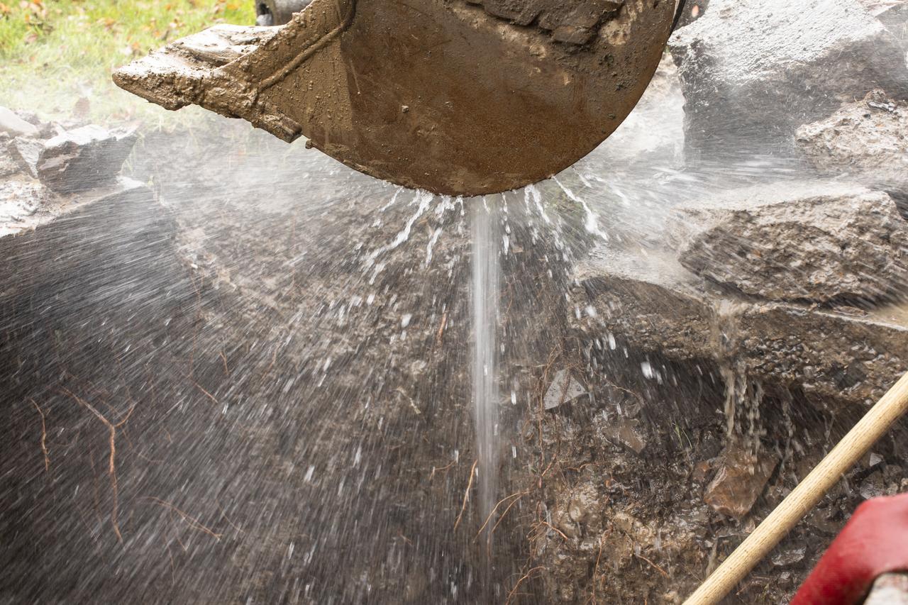 Water spraying from a leak in the ground and a digger above it