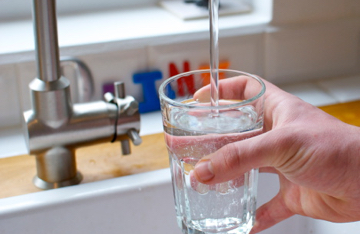 A person pouring a glass of water into a glass from a faucet 