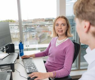 A graduate on a computer talking to another person